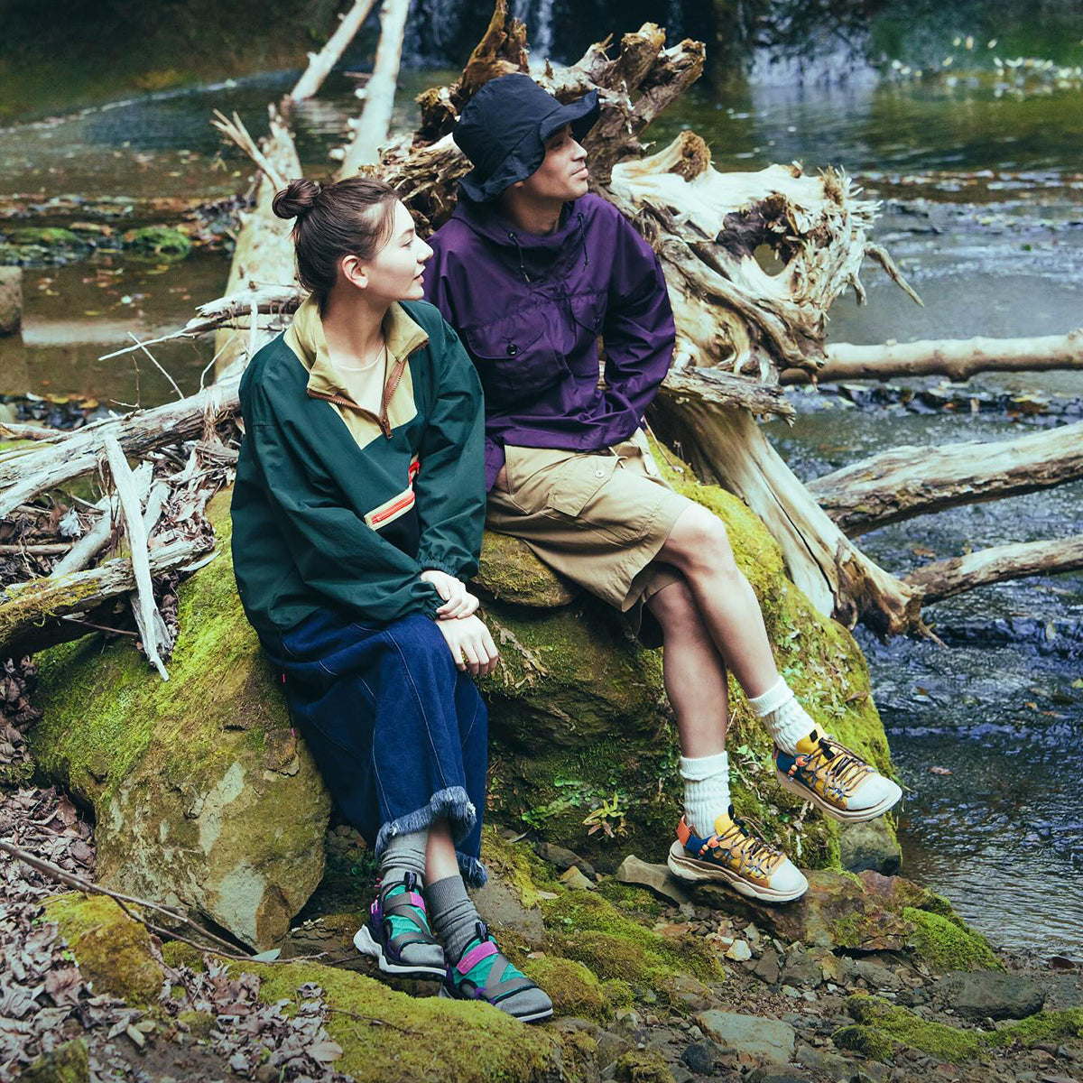 Flower MOUNTAIN (フラワーマウンテン) のイメージ画像。川の傍の岩に、アウトドアスタイルでFlower Mountain（フラワーマウンテン）のサンダルを履いた男女が腰かけている。