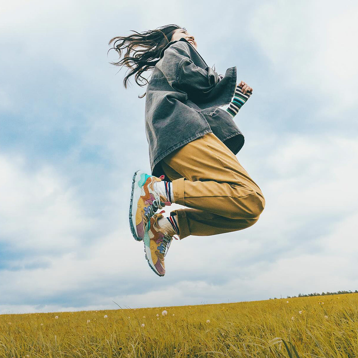 Flower MOUNTAIN (フラワーマウンテン) のイメージ画像。草原でFlower MOUNTAIN (フラワーマウンテン) のスニーカーを履いている女性がジャンプしている。